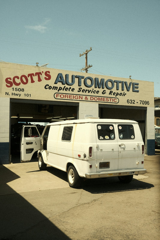 A white van is parked in front of an auto shop.